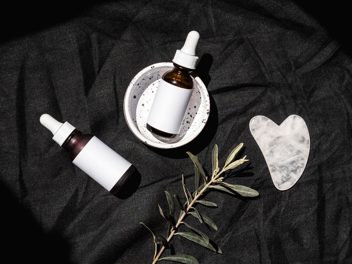 Unlabeled skincare serum bottles with a Gua Sha stone on dark fabric