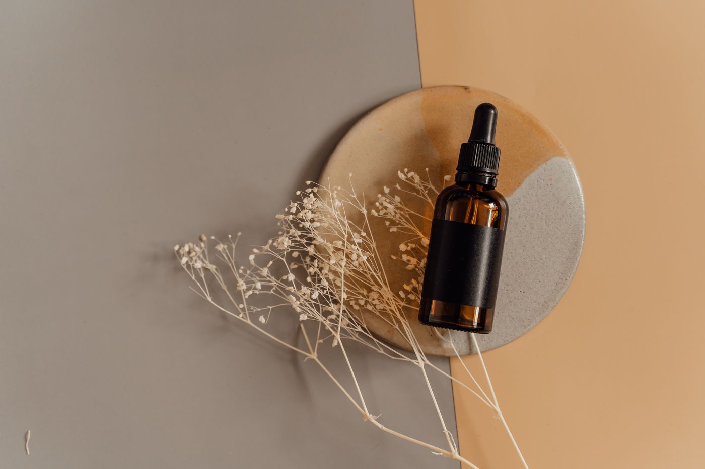 A plain amber dropper bottle styled with dried flowers