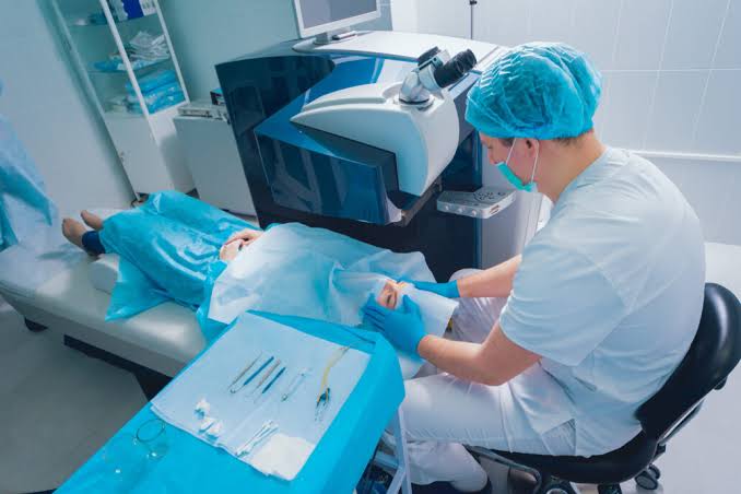A clinician in a surgical cap and mask preparing a patient for a procedure in a modern treatment room
