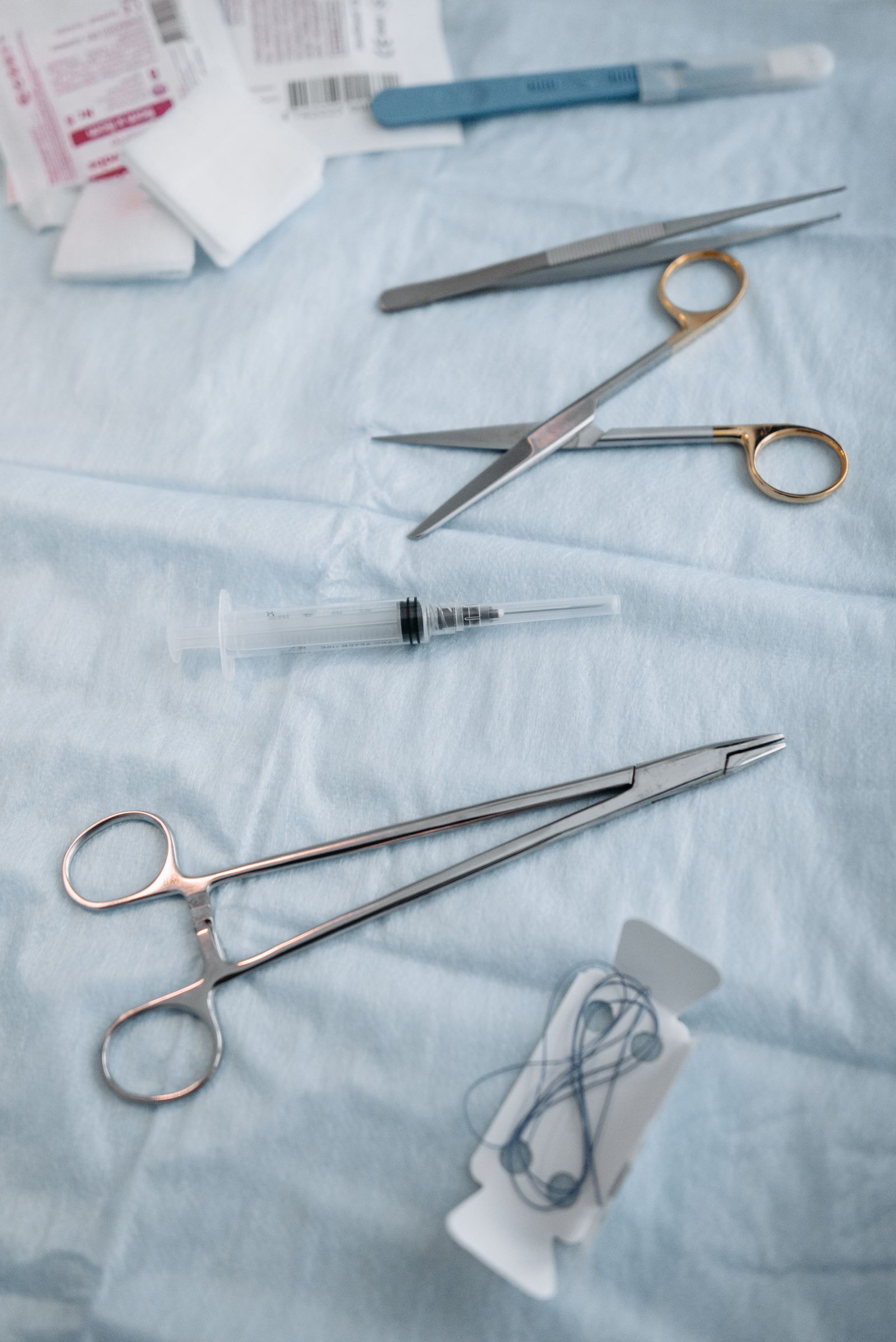 A needle holder, forceps, and a coil of fine surgical suture thread laid out for a minimally invasive procedure — stock photography, not an actual Plus253 setup